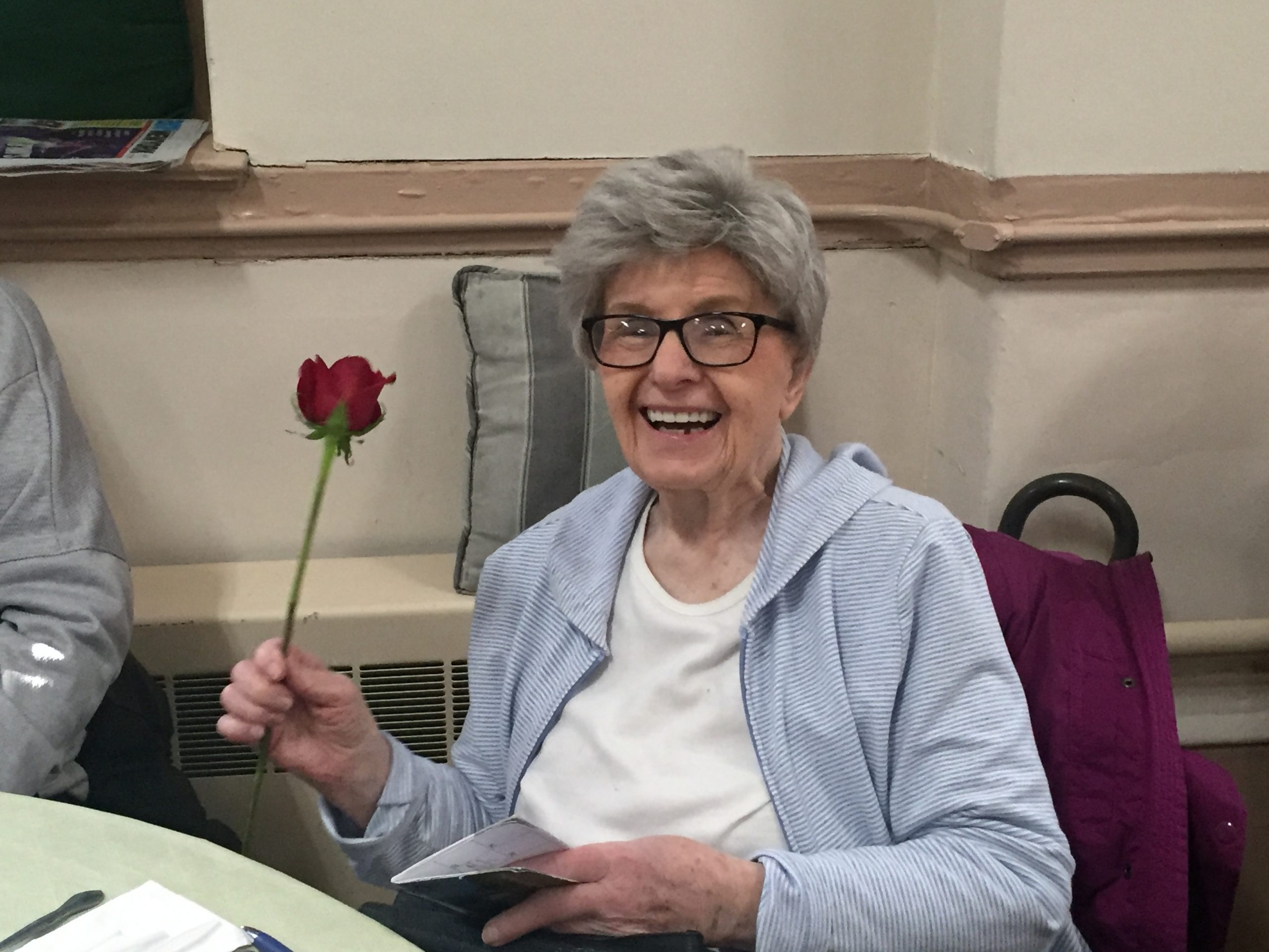 an elderly woman smiling and holding a rose for international woman's day 2019