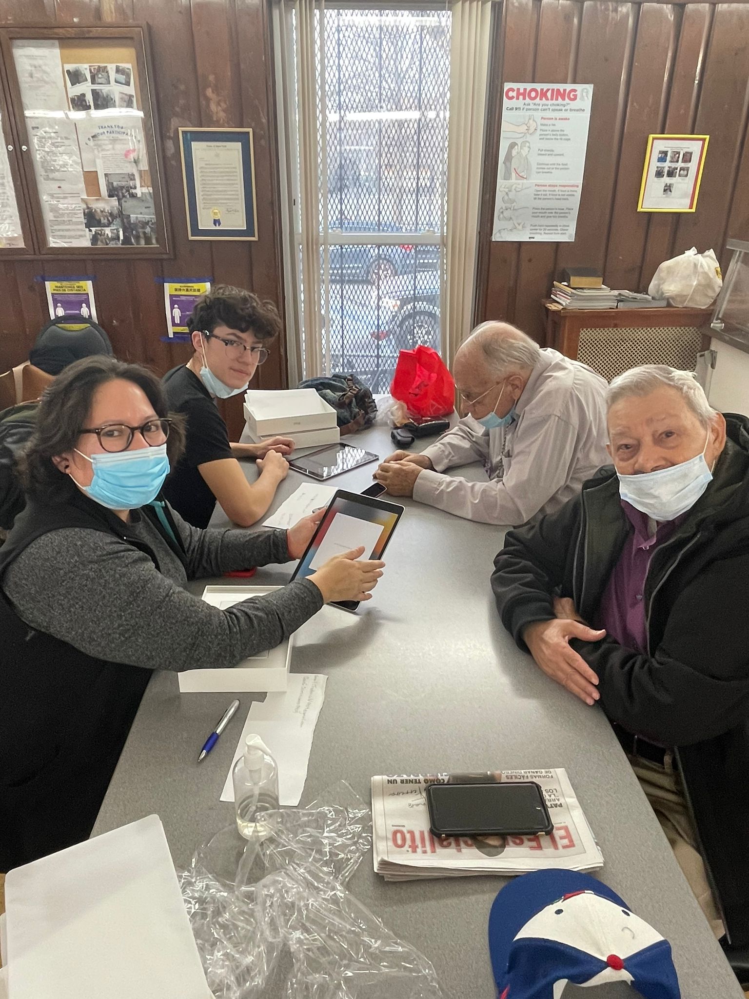 Two older adults sitting at a table with two individuals with iPads
