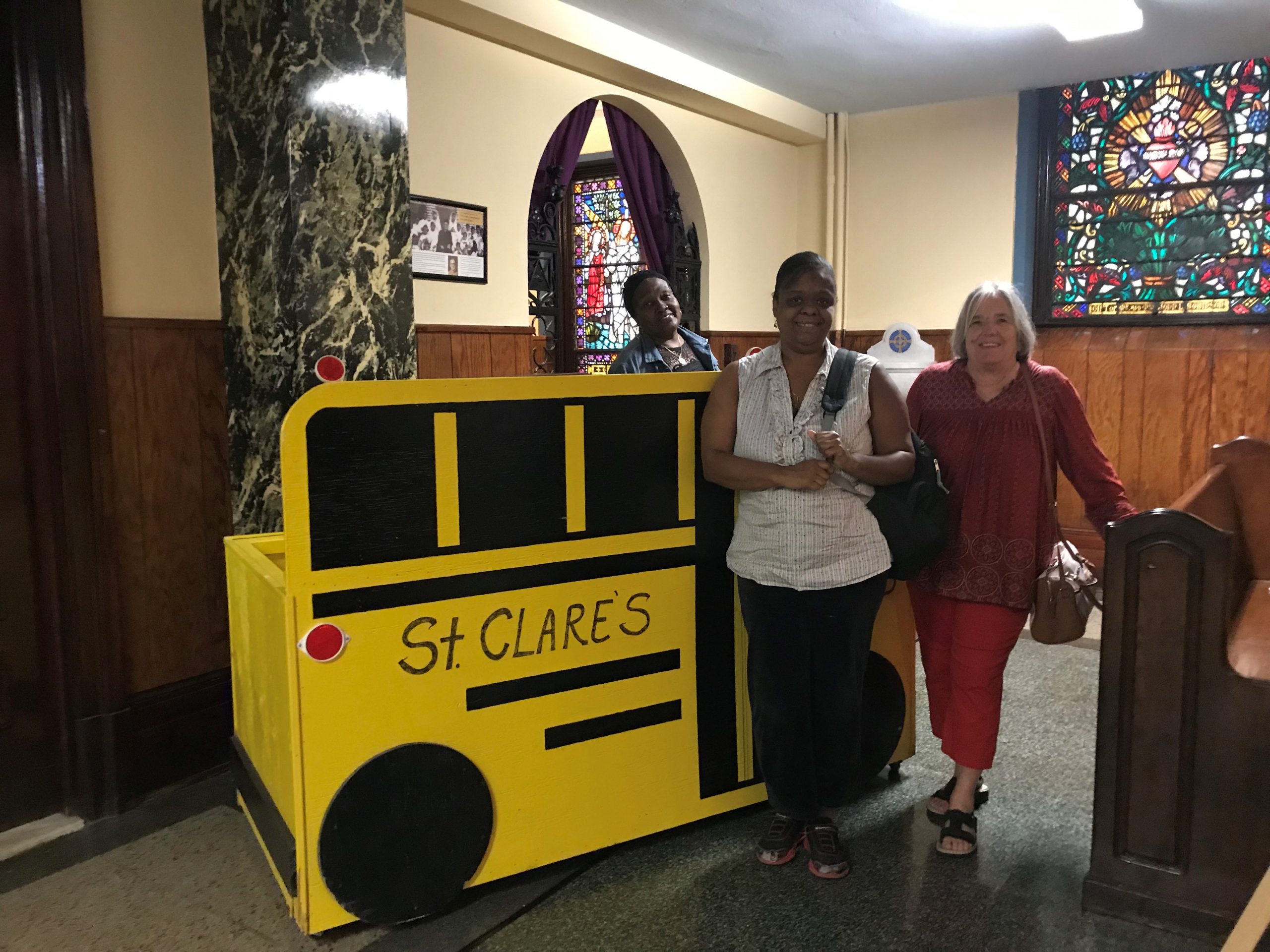 staff smiling in front of a wooden crafted bus for the back-to-school event and school supply donations