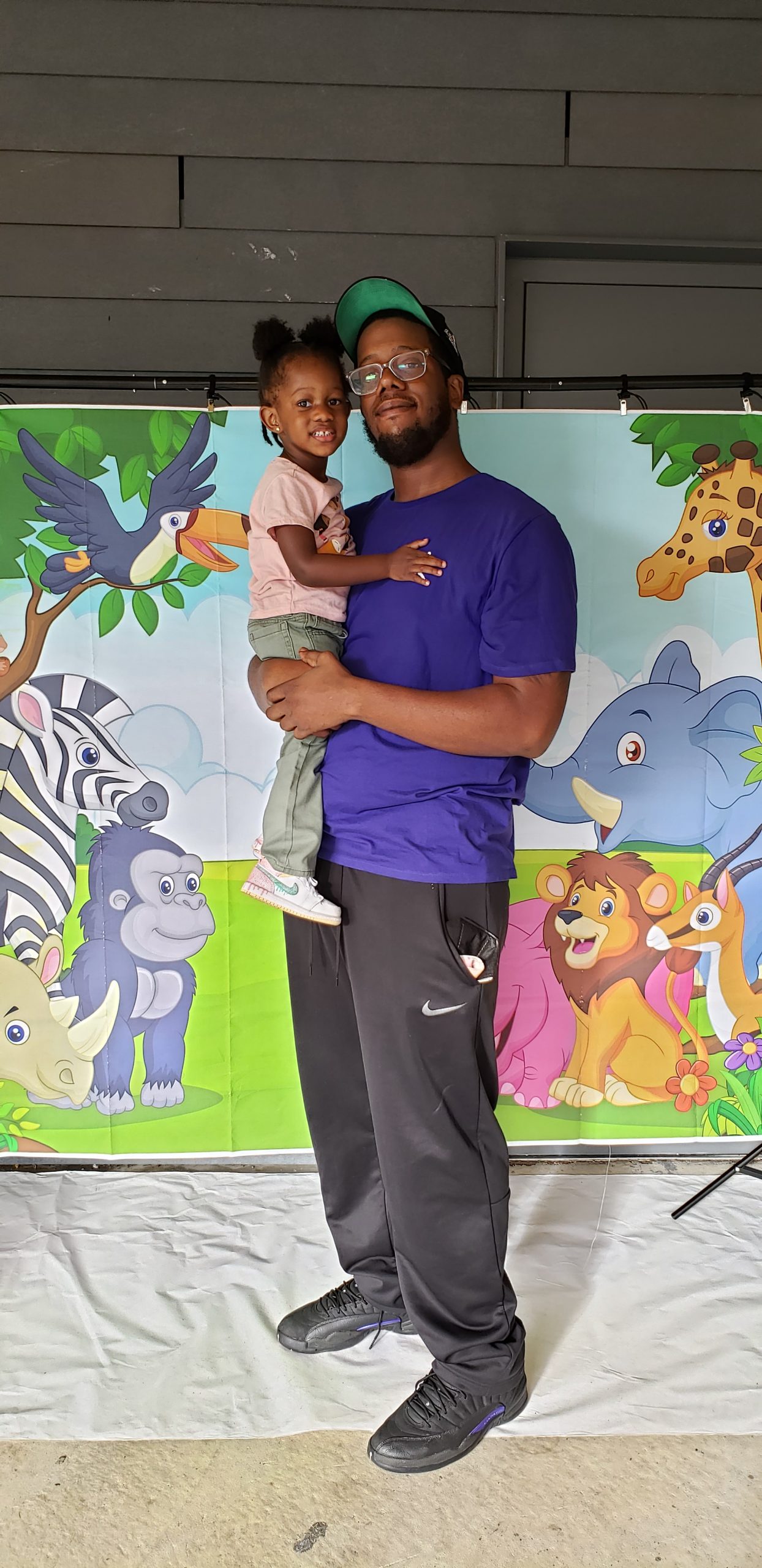 Male figure and their little one pose for a picture in front of animal-themed backdrop.
