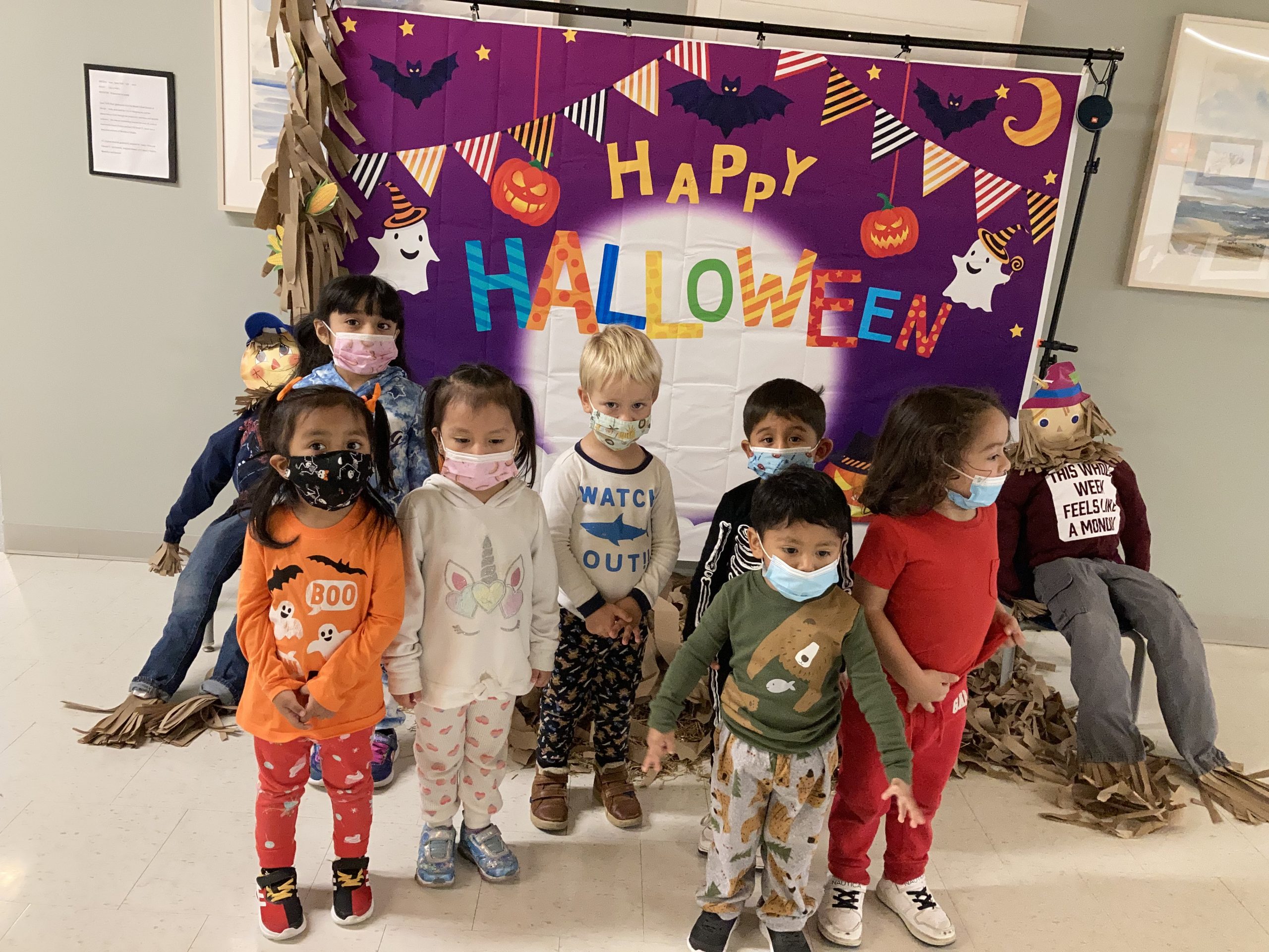 Students gather for a photo in their costumes in front of a Happy Halloween sign.
