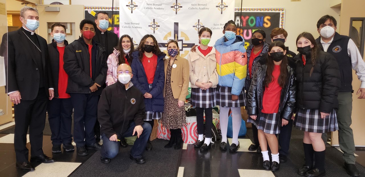 Bishop Brennan, St. Bernard students and Catholic Charities Brooklyn and Queens staff pose for a photo with donations from student-driven charity drive.