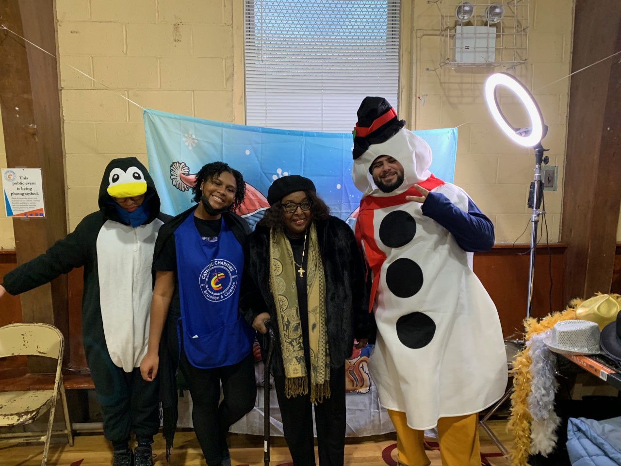 Four people pose for a photo. One person is dressed in a penguin costume. Another person is dressed in a snowman costume.